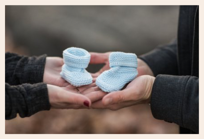 image depicting two parents to be holding knitted baby shoes